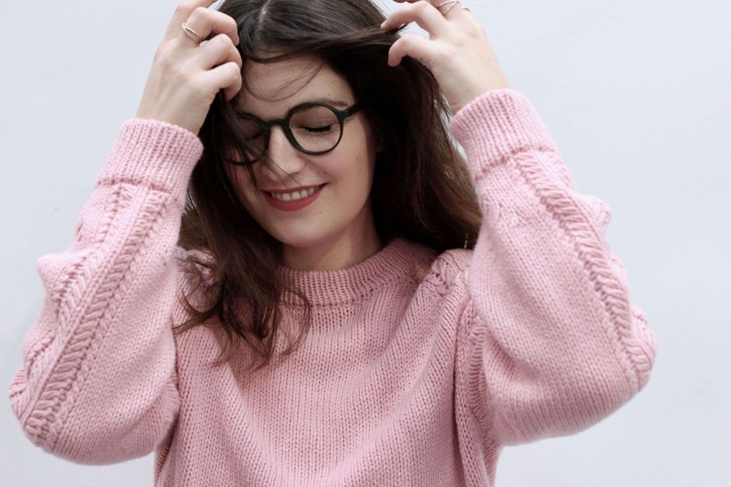 Eine Frau im rosa Pullover trägt eine individuelle Brille und freut sich.
